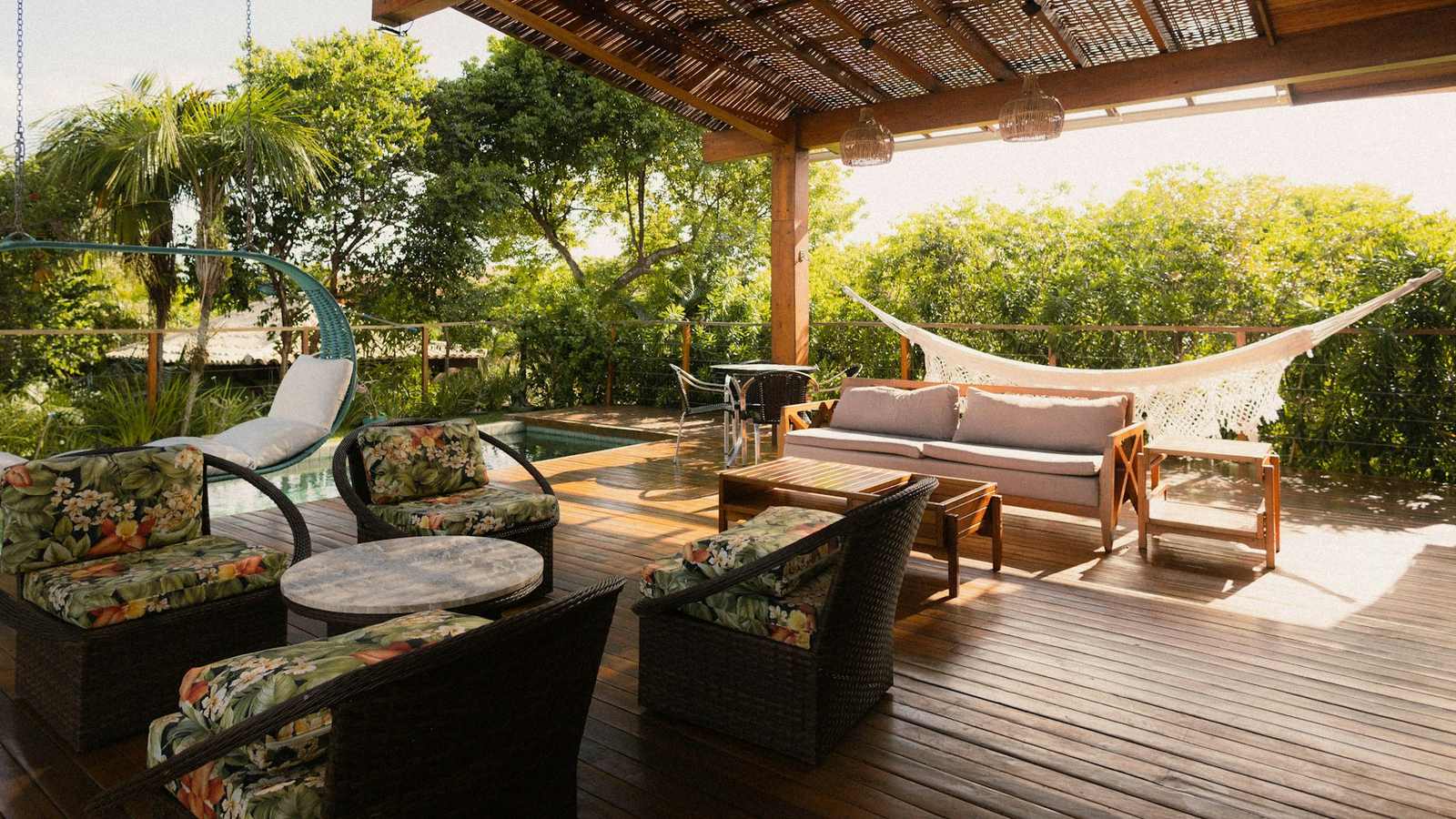 Covered wood deck outdoor living area with patio chairs, a hammock and a pool